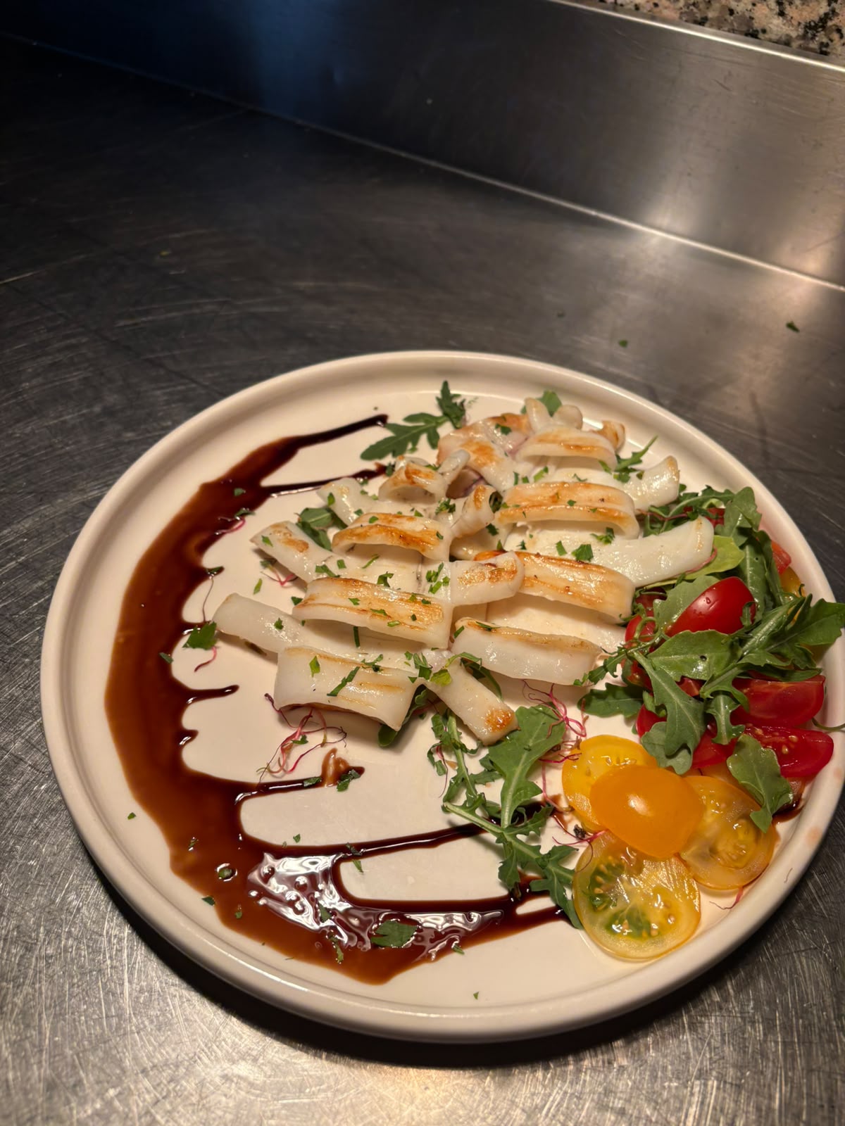 Calamari grigliati serviti con rucola, pomodorini e riduzione di aceto balsamico